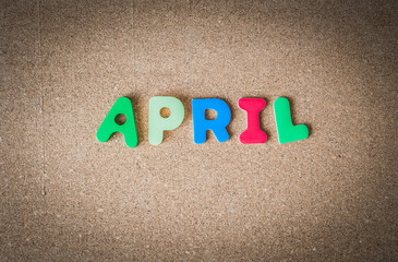 Colorful wooden word APRIL on cork board with selective focus