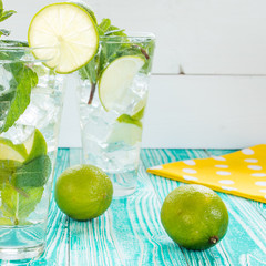 mojito in glasses with ice cubes,  decorated by mint leaf, lime fruits, yellow napkin at white polka dots on turquoise colored wooden table, top view
