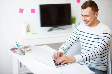 Cheerful smiling  guy sitting working on the laptop 