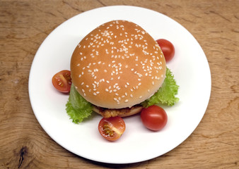 Appetizing homemade beef burger with salad and small tomatoes on white plate over wood background ready to eat
