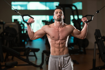 Fototapeta na wymiar Young Bodybuilder Exercising Biceps On Cable Machine