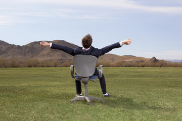 Businessman sitting on chair on green meadow