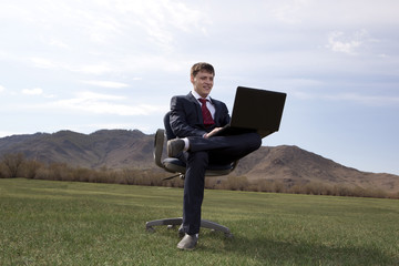 Businessman sitting on chair with a laptop on green meadow