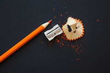 sharpener and orange pencil shavings on black - Powered by Adobe