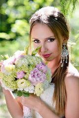 Fototapeta premium Beauty bride in bridal gown with bouquet and lace veil on the nature. Beautiful model girl in a white wedding dress. Female portrait in the park. Woman with hairstyle. Cute lady outdoors