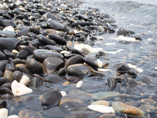 Obraz premium Sun reflections on pebble stones on the beach and sea water.