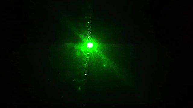 ein gr&uuml;ner Laser leuchte direkt in die Kamera in einem dunklen Raum