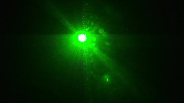 ein gr&uuml;ner Laser leuchte direkt in die Kamera in einem dunklen Raum