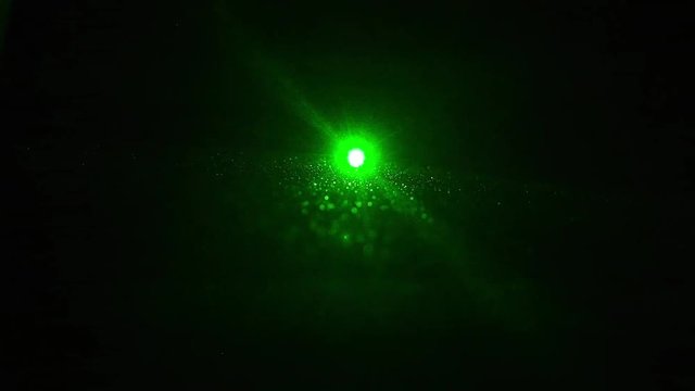 ein gr&uuml;ner Laser leuchte direkt in die Kamera in einem dunklen Raum