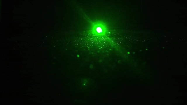 ein gr&uuml;ner Laser leuchte direkt in die Kamera in einem dunklen Raum