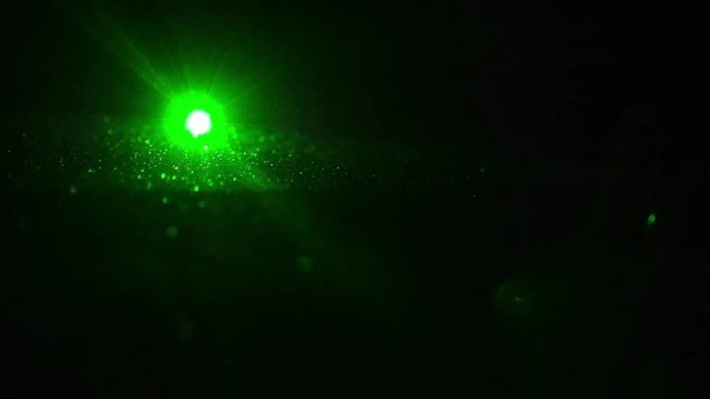 ein gr&uuml;ner Laser leuchte direkt in die Kamera in einem dunklen Raum