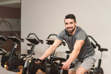 Fototapeta na wymiar Muscular Man Doing Cycling In Modern Fitness Center