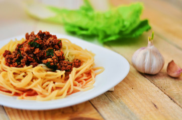 Spaghetti with meat in tomato sauce on a white plate. Garlic, salad and a plate of spaghetti on a wooden background