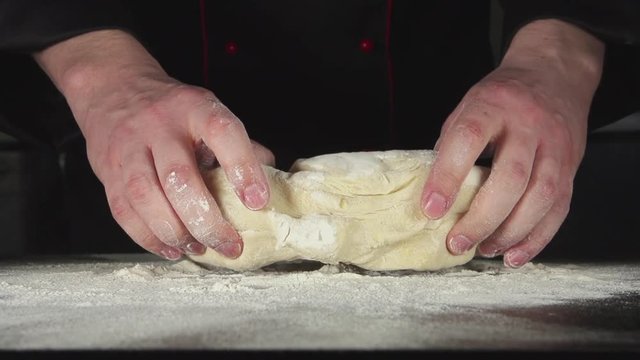 SLOW: A cook throws up and kneads a dough on a table in the kitchen