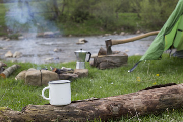 Mug stands on a log near the fire at a campsite.