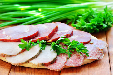 Sliced sausages on a wooden background. Green onions and parsley on a background