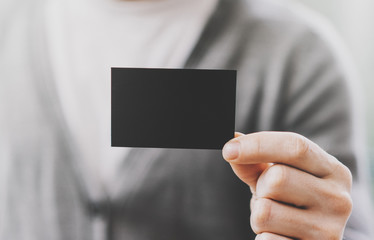 Man wearing casual shirt and showing empty black business card. Blurred background. Ready for private information. Horizontal mockup, fim effects