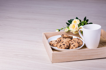 tray with chocolate chip cookies, tea and flowers on wooden back