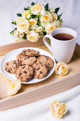 wooden tray with chocolate chip cookies, cup of tea and flowers