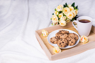 close up of wooden tray with chocolate chip cookies, cup of tea