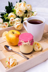 wooden tray with cup of tea, jam-jar, apple and flowers