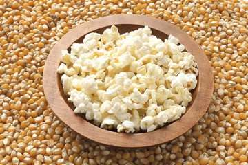 pop corn in wooden bowl with kernels on the background