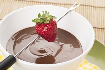 strawberry on fondue stick and melted chocolate bowl