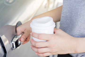 Woman holding white coffee cup and opening a car door, morning w