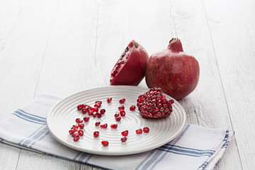 Pomegranate whole, half and seeds on white plate. Horizontal image with back lighting. Shallow depth of field.