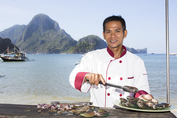 Filipino chef preparing a meal on the grill on the coast of El Nido