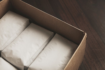 Closeup opened big carton box full of blank hermetic white packages with coffee or tea. Everything on red wooden table ready to sale or ship to distrubutors. Small business concept