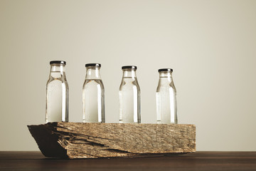 Obraz na płótnie Canvas Four clear transparent glass bottles with black caps filled with pure drinking water presented on wooden brick, isolated on white