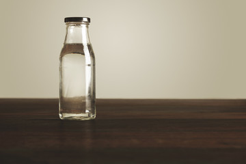 Clear transparent glass bottle with black cap filled with clean healthy drinking water presented on red wooden table, isolated on white