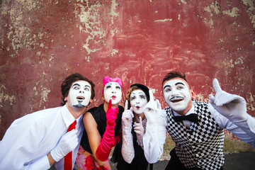 Four mimes point to the top on a red wall.