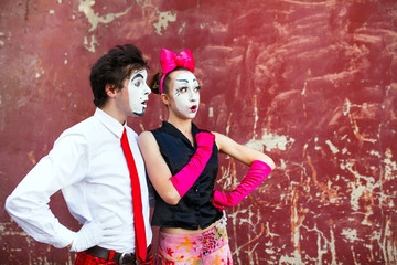 Couple mimes looking aside on the background of a red wall.
