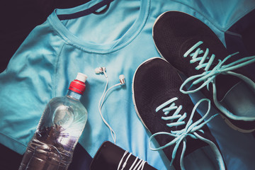 Sport equipment. Sneakers, bottle with water, phone with earphones, sportswear. Focused on sneakers. Lay shot.
