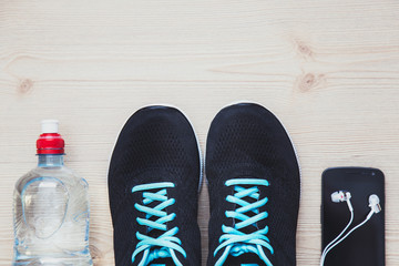 Sport equipment. Sneakers, bottle with water, phone with earphones on wooden background. Flat lay shot. Focused on sneakers.