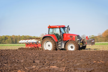 Ackerbau, roter Traktor mit rotem Pflug bei der Bodenbearbeitung