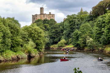 People rowing along the River Coquet by Warkworth Castle