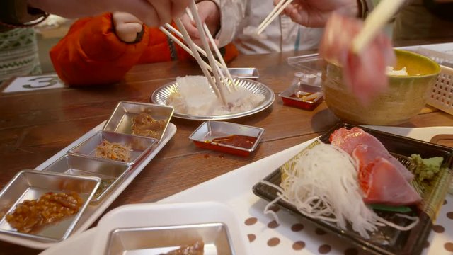 Hands of People With Chopsticks Eating Sashimi Sushi