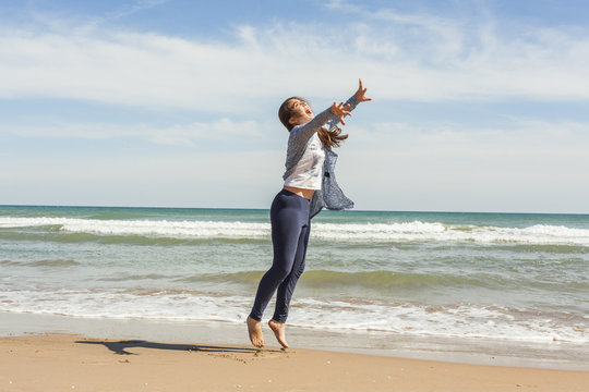 Full shot of a smily teenager jumping in the seashore of the bea