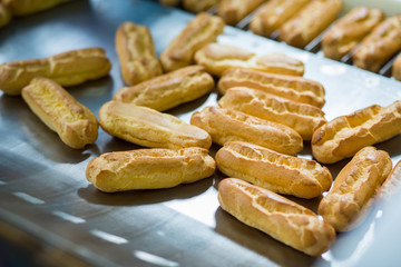 Eclair shells on metal surface. Yellow dough products. Ingredient for tasty dessert. Fresh baked goods at factory.