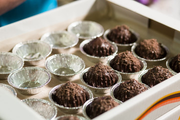 Brown sweets in small cups. Dark candies in white box. Time to pack the goods. Marketable condition of fresh dessert.