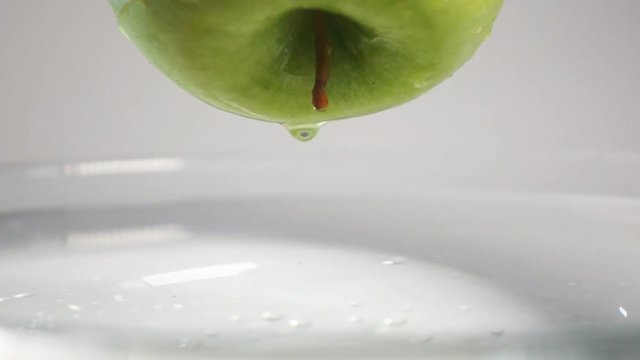 LIttle drop of water falling down from the fresh green apple into the water with small circular waves and little splash. Super slow motion shot on Sony rx 10 ii, white background isolated