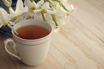 Narcissus flowers and cup of tea on a wooden table .