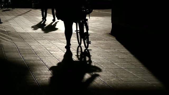 STOCKHOLM, SWEDEN, APR 2016: Silhouette woman walking and carrying her bike with shadow on the ground