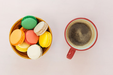 Coffe cup and colorful macaroons on pastel background, top view