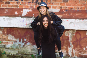 Two stylish and happy street girls posing at the wall. Sisters.