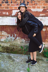 Fototapeta na wymiar Two stylish and happy street girls posing at the wall. Sisters.