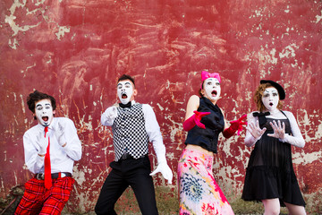 Four mimes standing in awe at the background of a red wall.